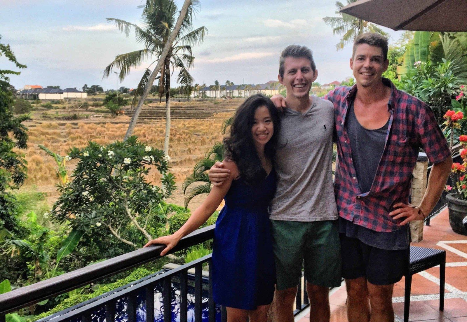Three friends smiling on a balcony above rice fields and palm trees