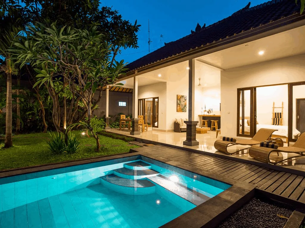 A typical Seminyak villa at dusk: a small pool, a wooden deck with loungers and an open living room