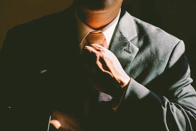 A man in a dark suit adjusting his tie in a shaft of light