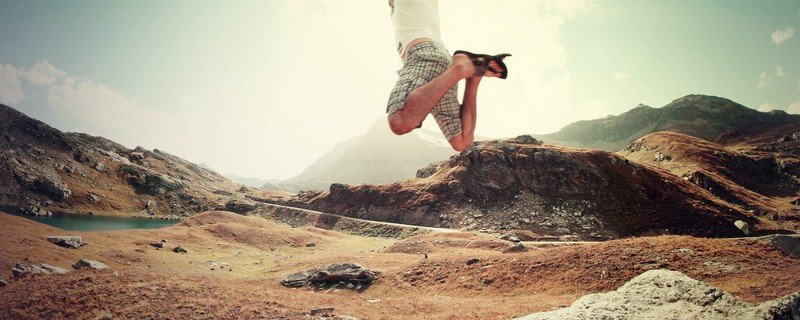 A person leaping high above a rocky mountain valley with a small lake