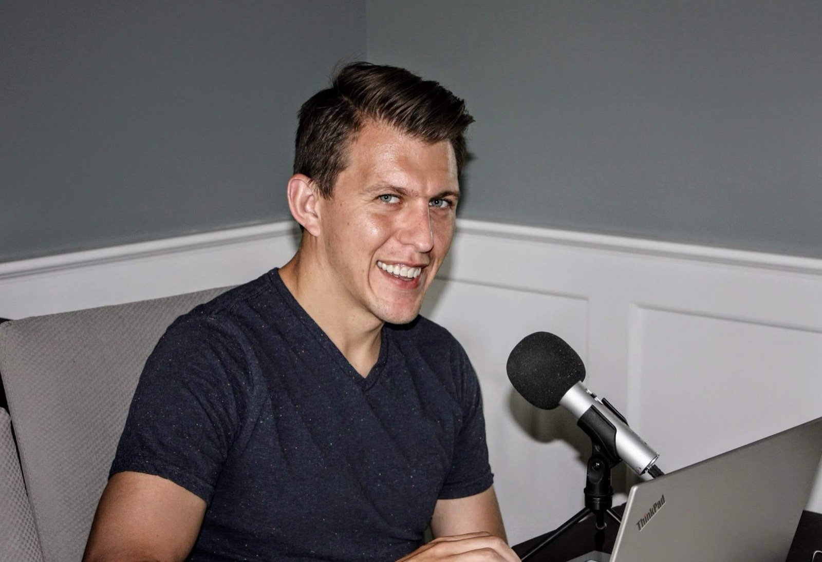 A smiling man at a podcast microphone and laptop